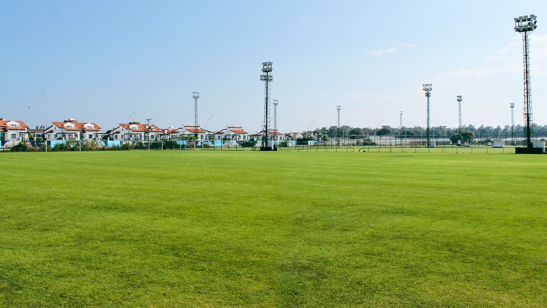 Limak Arcadia Hotel har en stor, velstelt gressplen som er perfekt for en fotballtreningsleir i Tyrkia, med høye lyskastere og synlige boligblokker under en klarblå himmel.