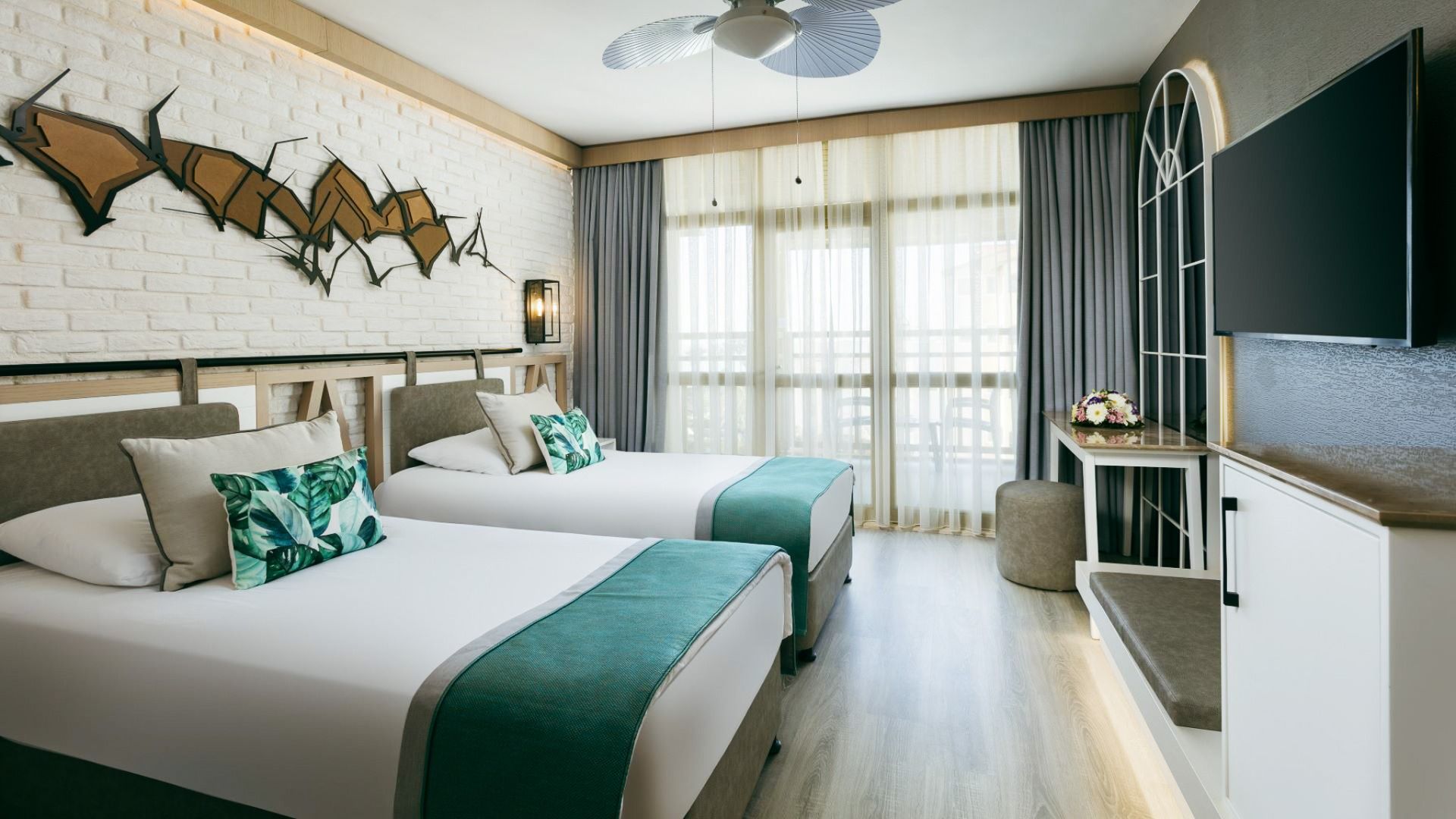 Moderne rom på Hotel Limak Arcadia med to enkeltsenger med blågrønt og hvitt sengetøy, stilige puter, veggkunst, et stort vindu med gjennomsiktige gardiner, flatskjerm-TV og et bord med blomster - gjenåpning 2026.