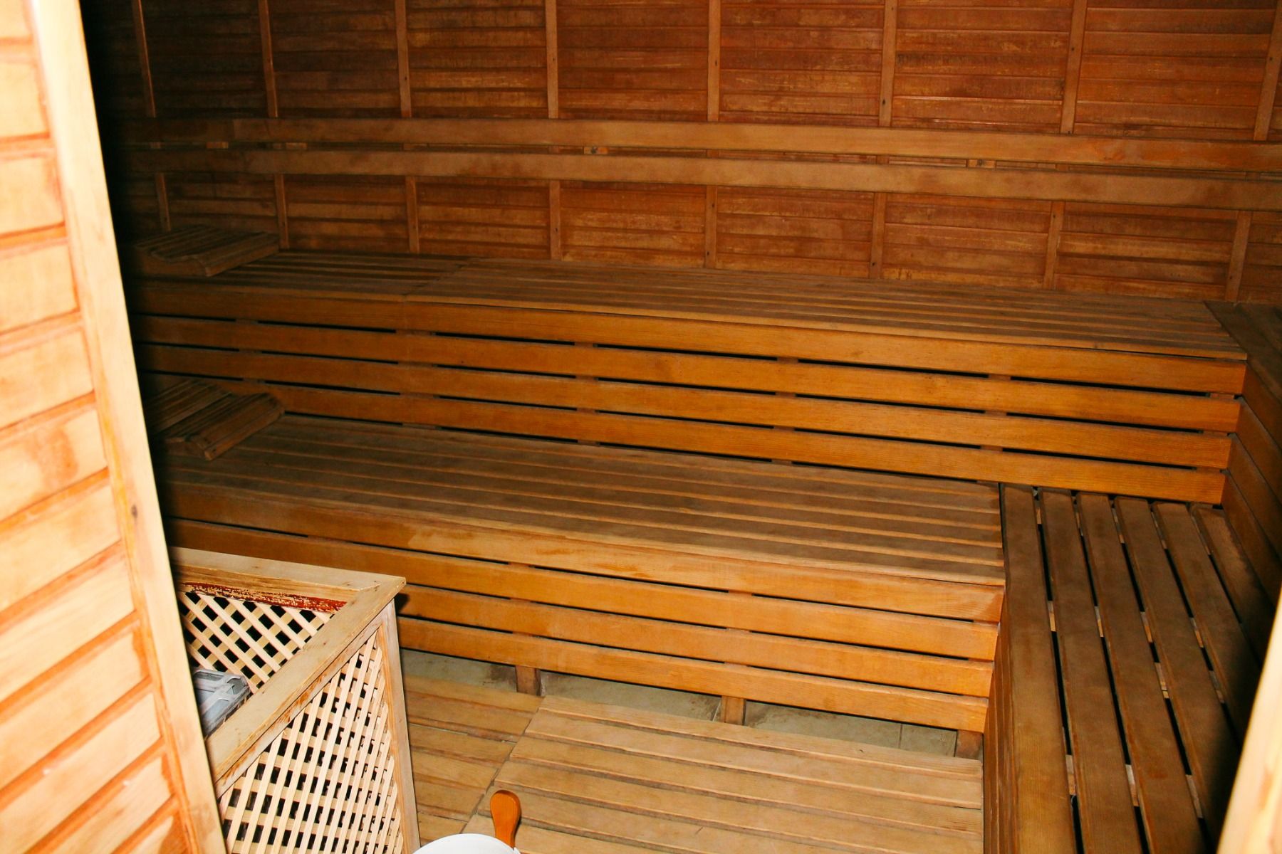 Linda Resort har et badstuerom i tre med benker i flere nivåer langs veggene og en kurv med badstueutstyr i forgrunnen.