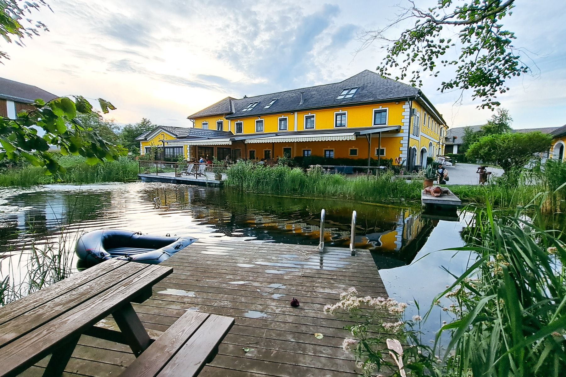 En knallgul bygning i Neuhofen an der Ybbs med brygge, stige og svart gummibåt ligger ved et stille tjern på landsbygda - det er et syn man nyter på det familiedrevne Hotel Perbersdorfer Heuriger.