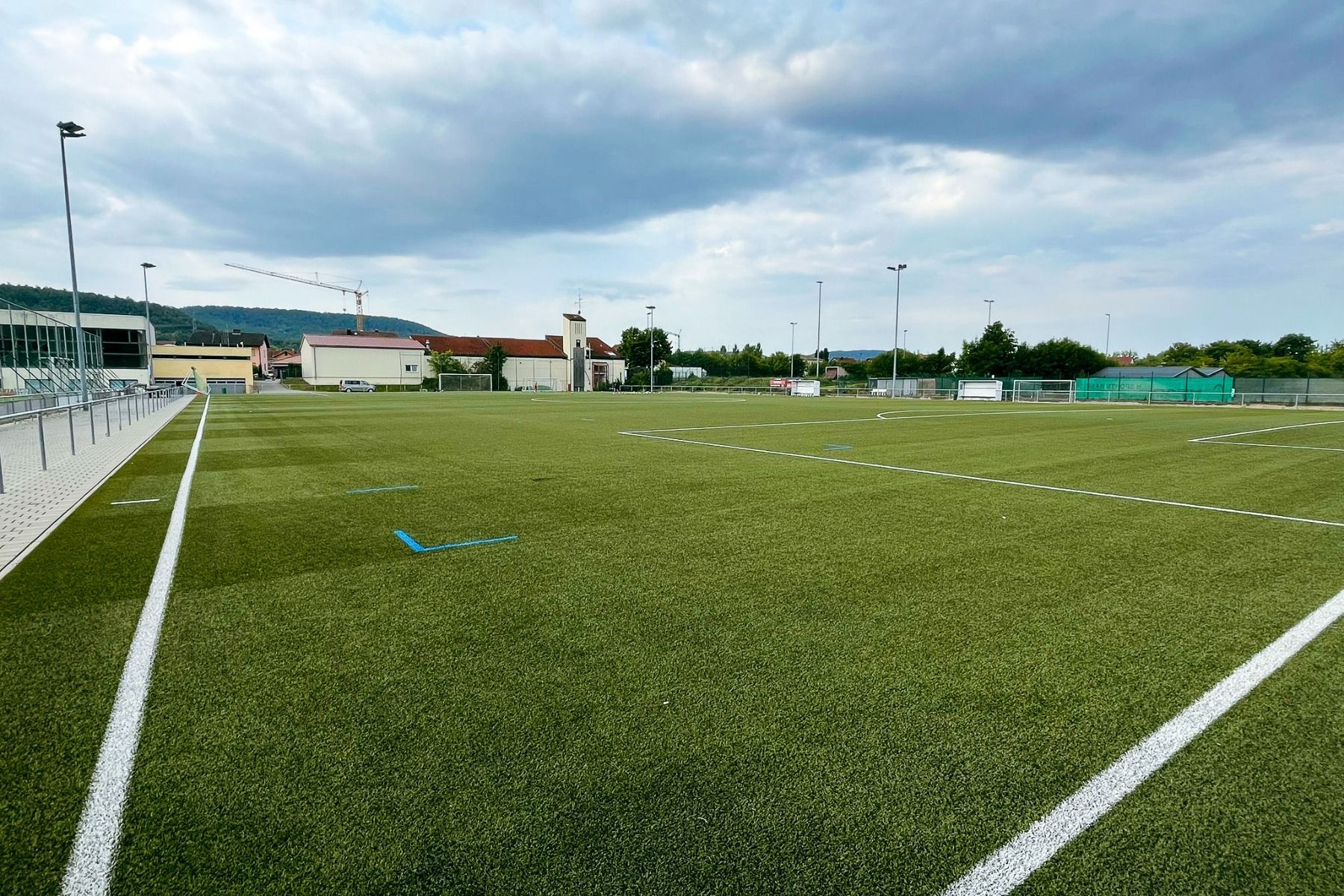 Ein leerer Fußballplatz mit Kunstrasen und weißen Linien unter einem wolkenverhangenen Himmel, umgeben von Gebäuden, Lichtern und Bäumen - nur wenige Schritte vom Weingut Hotel Goger und seiner berühmten fränkischen Küche entfernt.