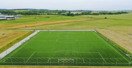 Luftaufnahme des Hotels Primavera mit einem Parkplatz davor, umgeben von Gr&uuml;nfl&auml;chen und Wohngeb&auml;uden unter einem teilweise bew&ouml;lkten Himmel.