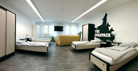 Zwei weiße Lieferwagen mit dem Schriftzug "The Wolfpack" parken vor einem Wohngebäude mit der Aufschrift Sportcampus Schlotheim, das für seine geräumigen Zimmer und ein modernes Fitnessstudio bekannt ist. Blauer Himmel und Bäume rahmen die Szene ein.