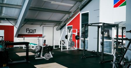 Zwei weiße Lieferwagen mit dem Schriftzug "The Wolfpack" parken vor einem Wohngebäude mit der Aufschrift Sportcampus Schlotheim, das für seine geräumigen Zimmer und ein modernes Fitnessstudio bekannt ist. Blauer Himmel und Bäume rahmen die Szene ein.