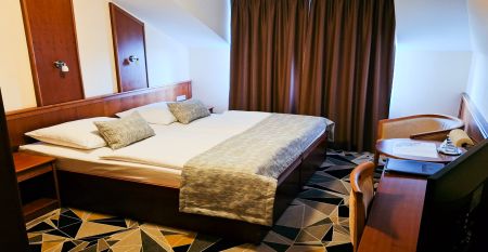 Luftaufnahme des Hotels Primavera mit einem Parkplatz davor, umgeben von Gr&uuml;nfl&auml;chen und Wohngeb&auml;uden unter einem teilweise bew&ouml;lkten Himmel.