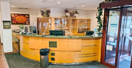 Luftaufnahme des Hotels Primavera mit einem Parkplatz davor, umgeben von Gr&uuml;nfl&auml;chen und Wohngeb&auml;uden unter einem teilweise bew&ouml;lkten Himmel.