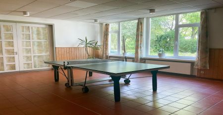 Ein verschn&ouml;rkelter schwarzer Metallbogen mit einer h&auml;ngenden Laterne steht am Eingang des Parks in der N&auml;he eines wei&szlig;en Geb&auml;udes mit rotem Ziegeldach und B&auml;umen - ideal f&uuml;r Besucher, die zum G&auml;stehaus Northeim wollen oder auf der Suche nach nahe gelegen