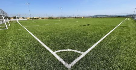 Luftaufnahme des Hotels Primavera mit einem Parkplatz davor, umgeben von Gr&uuml;nfl&auml;chen und Wohngeb&auml;uden unter einem teilweise bew&ouml;lkten Himmel.