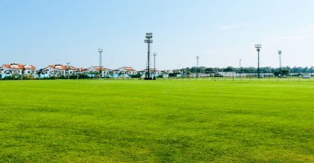 Luftfoto av Limak Arcadia Hotel med bassenger, hager, idrettsbaner og strandhytter - ideelt for fotballtreningsleiren i Tyrkia - omgitt av palmer og fjell under en klar himmel.