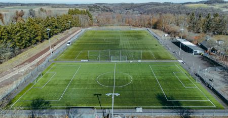 Das G&auml;stehaus Nettersheim ist ein modernes, dreist&ouml;ckiges Geb&auml;ude mit gro&szlig;en Fenstern, einer roten unteren Fassade, h&ouml;lzernen Obergeschossen und einem kleinen Balkon, eingebettet in eine gr&uuml;ne, nat&uuml;rliche Umgebung mit B&auml;umen unter der Sonne.