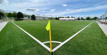 Zwei weiße Lieferwagen mit dem Schriftzug "The Wolfpack" parken vor einem Wohngebäude mit der Aufschrift Sportcampus Schlotheim, das für seine geräumigen Zimmer und ein modernes Fitnessstudio bekannt ist. Blauer Himmel und Bäume rahmen die Szene ein.
