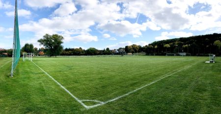 Zwei wei&szlig;e Lieferwagen mit dem Schriftzug "The Wolfpack" parken vor einem Wohngeb&auml;ude mit der Aufschrift Sportcampus Schlotheim, das f&uuml;r seine ger&auml;umigen Zimmer und ein modernes Fitnessstudio bekannt ist. Blauer Himmel und B&auml;ume rahmen die Szene ein.