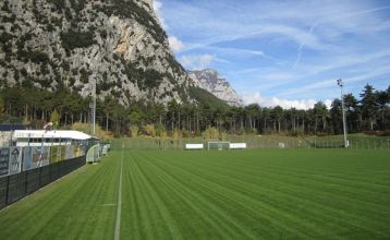 Luftaufnahme des Hotels Everest***, eines rosafarbenen mehrstöckigen Gebäudes mit renovierten Zimmern, umgeben von Grünanlagen, einer kleinen Kirche, Häusern, Gärten, bewaldeten Hügeln und nahe gelegenen Fußball- und Trainingsplätzen, die sich in die frie