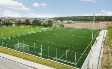 Luftaufnahme des Parkhotels mit Sonnenkollektoren, Außenpool, Tennisplätzen, Fitnessstudio und großem Parkplatz inmitten von Bäumen nahe dem Stadtzentrum von Pilsen an einem sonnigen Tag.