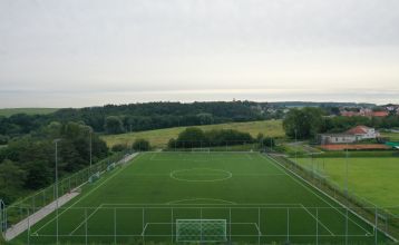 Luftaufnahme des Parkhotels mit Sonnenkollektoren, Außenpool, Tennisplätzen, Fitnessstudio und großem Parkplatz inmitten von Bäumen nahe dem Stadtzentrum von Pilsen an einem sonnigen Tag.