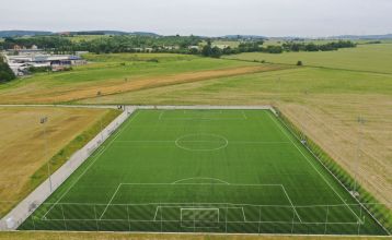 Luftaufnahme des Parkhotels mit Sonnenkollektoren, Außenpool, Tennisplätzen, Fitnessstudio und großem Parkplatz inmitten von Bäumen nahe dem Stadtzentrum von Pilsen an einem sonnigen Tag.
