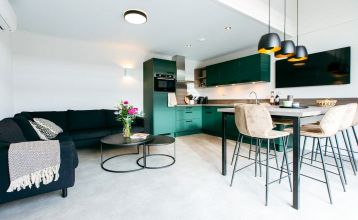 Modernes zweistöckiges Haus mit Metalldach, großen Fenstern und gelben Holzverkleidungen. Überdachte Terrasse mit Gartenmöbeln und Essbereich mit Blick auf einen grünen Rasen - perfekt zum Entspannen nach einem Tag in Duinrell.