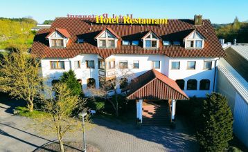 Hotel Empfinger Hof, med rødt tegltak og kvistevinduer, ønsker gjester velkommen til Fußballtrainingslager. Et "Hotel Restaurant"-skilt kroner bygningen, med trær og en asfaltert inngang som tilbyr gute Verpflegung og solrik varme.