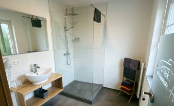 Luftaufnahme des Breitenberger Hofs*** mit Sonnenkollektoren und einem Wellnessbereich auf dem Dach, umgeben von geparkten Autos und Häusern in einer kleinen, hügeligen Stadt bei Passau. Auf dem Boden sind Schneeflecken zu sehen.