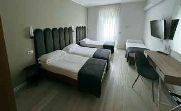 Luftaufnahme des Hotels Everest***, eines rosafarbenen mehrstöckigen Gebäudes mit renovierten Zimmern, umgeben von Grünanlagen, einer kleinen Kirche, Häusern, Gärten, bewaldeten Hügeln und nahe gelegenen Fußball- und Trainingsplätzen, die sich in die frie