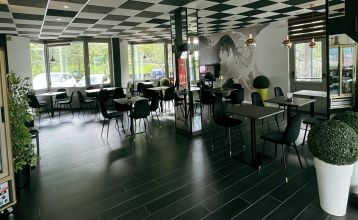 Luftaufnahme des Hotels Everest***, eines rosafarbenen mehrstöckigen Gebäudes mit renovierten Zimmern, umgeben von Grünanlagen, einer kleinen Kirche, Häusern, Gärten, bewaldeten Hügeln und nahe gelegenen Fußball- und Trainingsplätzen, die sich in die frie