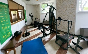 Luftaufnahme des Hotels Everest***, eines rosafarbenen mehrstöckigen Gebäudes mit renovierten Zimmern, umgeben von Grünanlagen, einer kleinen Kirche, Häusern, Gärten, bewaldeten Hügeln und nahe gelegenen Fußball- und Trainingsplätzen, die sich in die frie