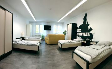 Zwei weiße Lieferwagen mit dem Schriftzug "The Wolfpack" parken vor einem Wohngebäude mit der Aufschrift Sportcampus Schlotheim, das für seine geräumigen Zimmer und ein modernes Fitnessstudio bekannt ist. Blauer Himmel und Bäume rahmen die Szene ein.