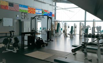 Zwei weiße Lieferwagen mit dem Schriftzug "The Wolfpack" parken vor einem Wohngebäude mit der Aufschrift Sportcampus Schlotheim, das für seine geräumigen Zimmer und ein modernes Fitnessstudio bekannt ist. Blauer Himmel und Bäume rahmen die Szene ein.