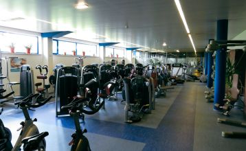 Der Gasthof & Gästehaus Trummer, ein hellblauer Gasthof mit rotem Dach, steht an einer von Bäumen gesäumten Straße nahe der Sportanlage Ritzing. Bei teilweise bewölktem Himmel sind parkende Autos und andere Häuser in der Nähe.