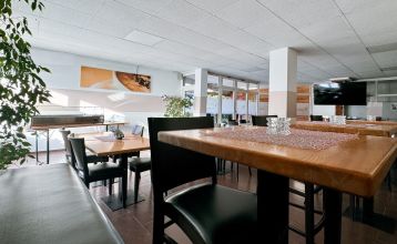 Der Sportpark Fun4You bietet einen hellen, leeren Besprechungsraum mit ovalen Holztischen, schwarzen Stühlen, gefliestem Boden, großen Fenstern und einem Bundesliga-Schild - ideal für Teambuilding vor einem Besuch im nahe gelegenen Idrettsparken. Deckenpr