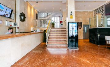 Vor dem Hotel Torremolinos Centro, einem vierstöckigen Gebäude mit Balkonen und geschlossenen Schaufenstern im Erdgeschoss, steht an einem sonnigen Tag eine Reihe von Topfbäumen.