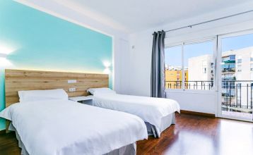 Vor dem Hotel Torremolinos Centro, einem vierstöckigen Gebäude mit Balkonen und geschlossenen Schaufenstern im Erdgeschoss, steht an einem sonnigen Tag eine Reihe von Topfbäumen.