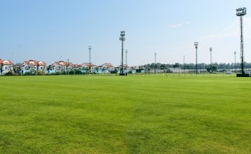 Luftfoto av Limak Arcadia Hotel, et livlig strandkompleks med bassenger, tennisbaner, hager, sandstrand med parasoller og brygge - ideelt for en fotballtreningsleir i Tyrkia. Omgitt av tette trær.