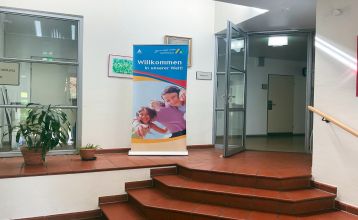 Ein verschnörkelter schwarzer Metallbogen mit einer hängenden Laterne steht am Eingang des Parks in der Nähe eines weißen Gebäudes mit rotem Ziegeldach und Bäumen - ideal für Besucher, die zum Gästehaus Northeim wollen oder auf der Suche nach nahe gelegen