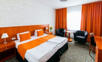 Luftaufnahme des Parkhotels mit Sonnenkollektoren, Außenpool, Tennisplätzen, Fitnessstudio und großem Parkplatz inmitten von Bäumen nahe dem Stadtzentrum von Pilsen an einem sonnigen Tag.