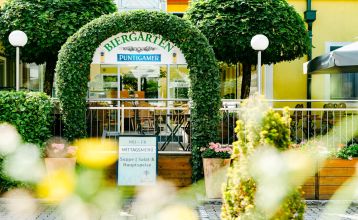 Hotell- og restaurant Schachenwald er en strålende gul, toetasjes bygning med rødt takstein under blå himmel – ideelt for treningsleirer – med potteplanter ved inngangen og biler parkert på den brosteinsbelagte oppkjørselen.