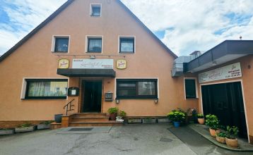 En ferskenfarget toetasjes bygning, Gasthof Kapellenhof, har skilt med ordene Gästehof Kleinlandhof over døren og garasjen. Potteplanter står langs inngangspartiet og skaper en koselig atmosfære under den overskyede himmelen.