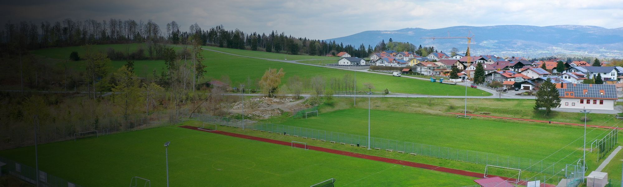 Kunstrasen-Fu&szlig;ballplatz auf Sardinien mit markierten Spielfeldlinien und Umz&auml;unung, im Hintergrund Berge und Geb&auml;ude.