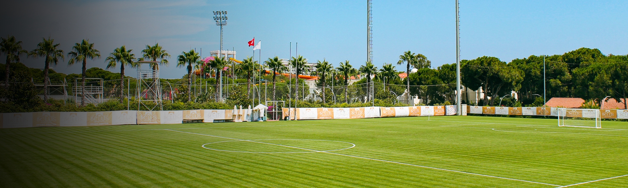 Perfekter Fu&szlig;ballplatz in Belek, umgeben von Palmen und Flutlichtmasten.