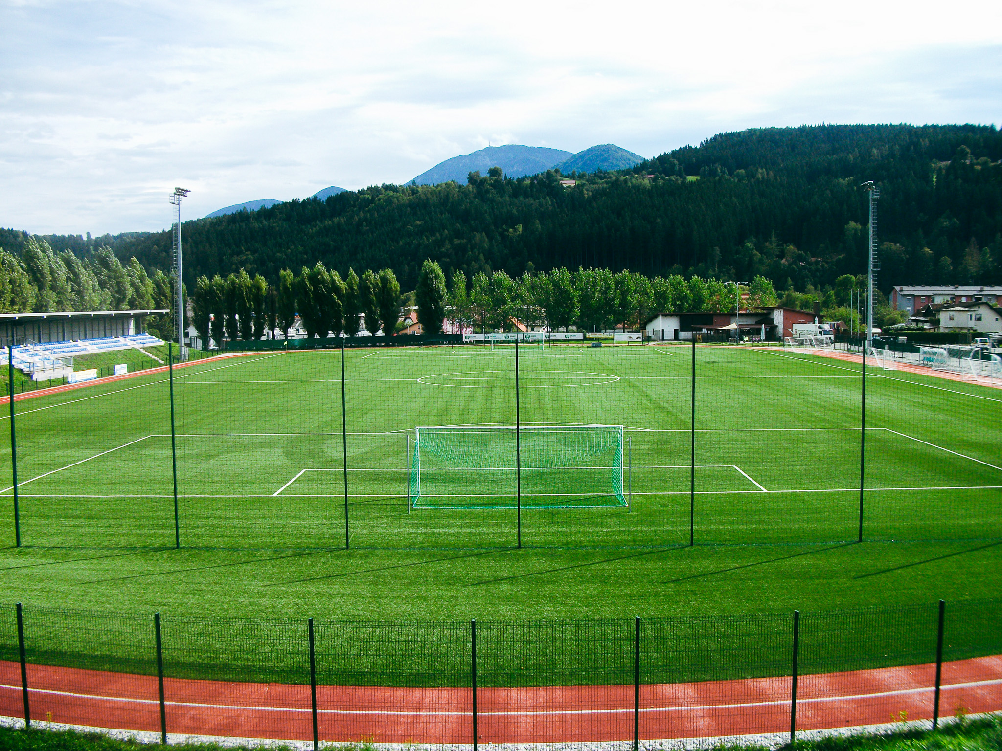 Fu&szlig;ballplatz in K&auml;rnten, eingebettet in eine idyllische Alpenkulisse mit Trib&uuml;ne und Trainingsinfrastruktur.