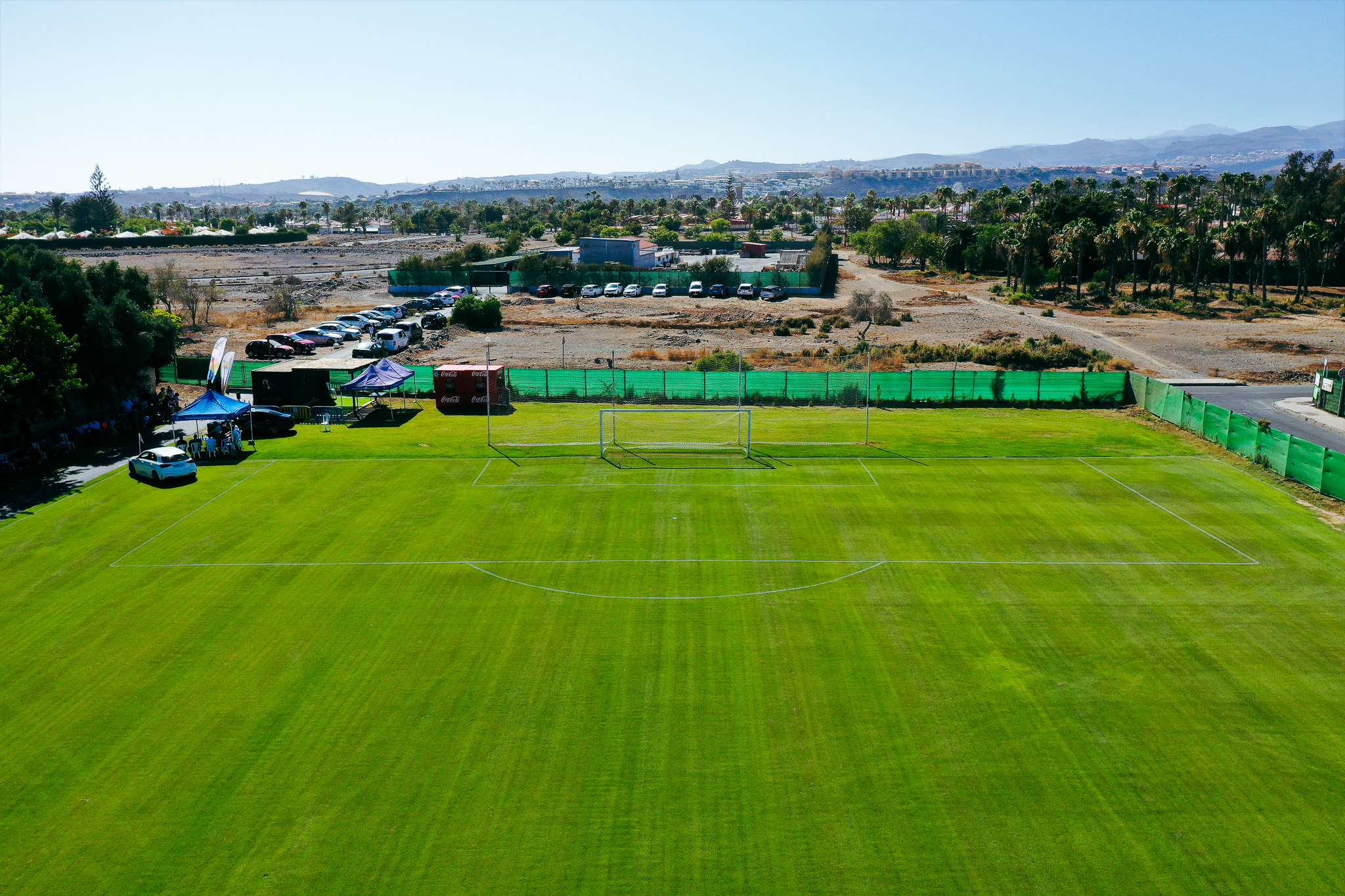 Ein idyllisches Spielfeld mit Naturrasen, eingerahmt von Palmen und weiten Landschaften.