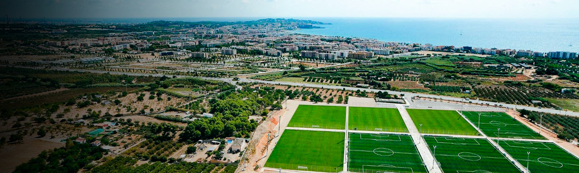 Eine moderne Sportanlage mit mehreren Fu&szlig;ballfeldern, K&uuml;stenaussicht und urbaner Umgebung.