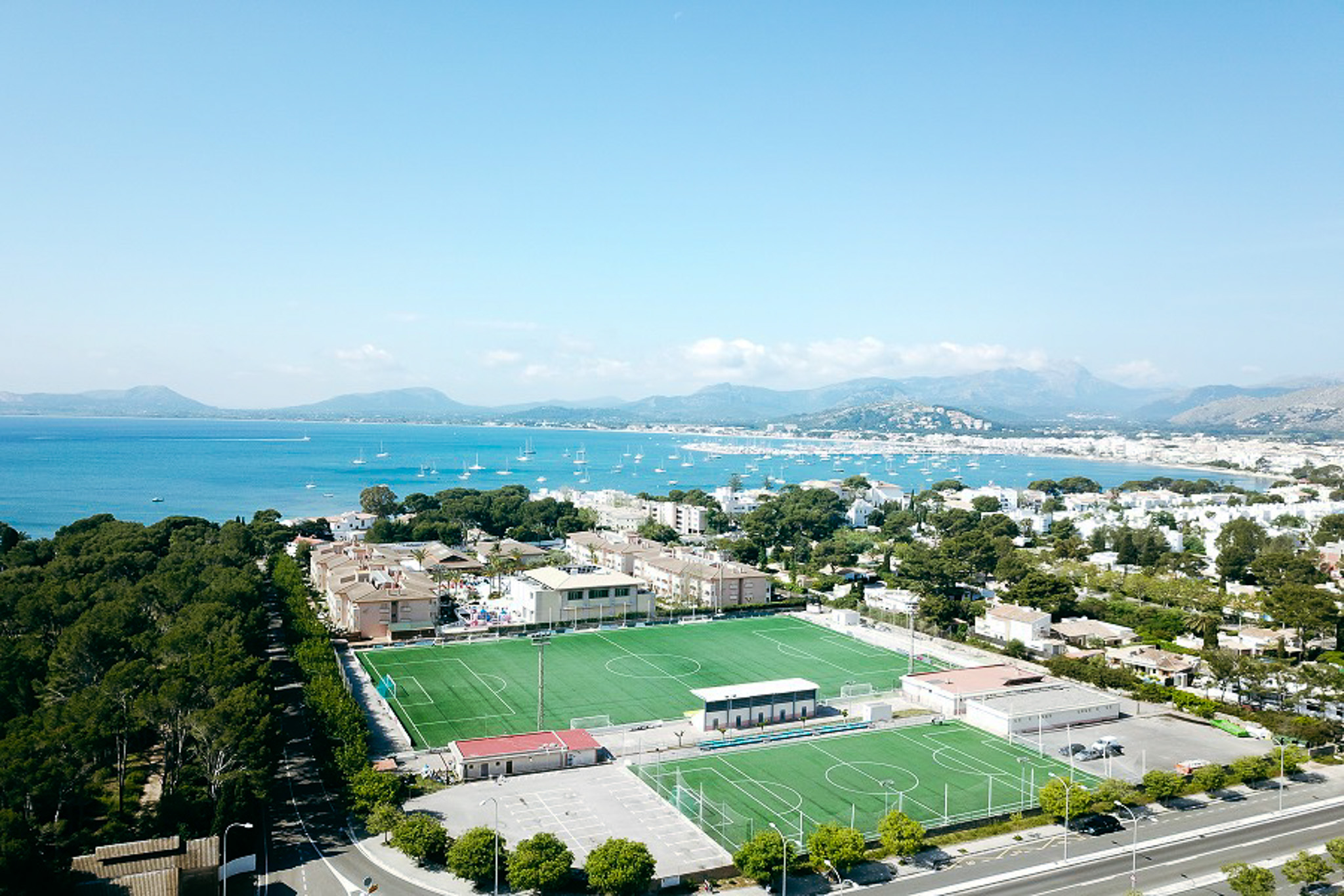 Ein direkt am Meer gelegener Fu&szlig;ballplatz mit traumhafter Kulisse, Bergen und Segelbooten im Hintergrund.