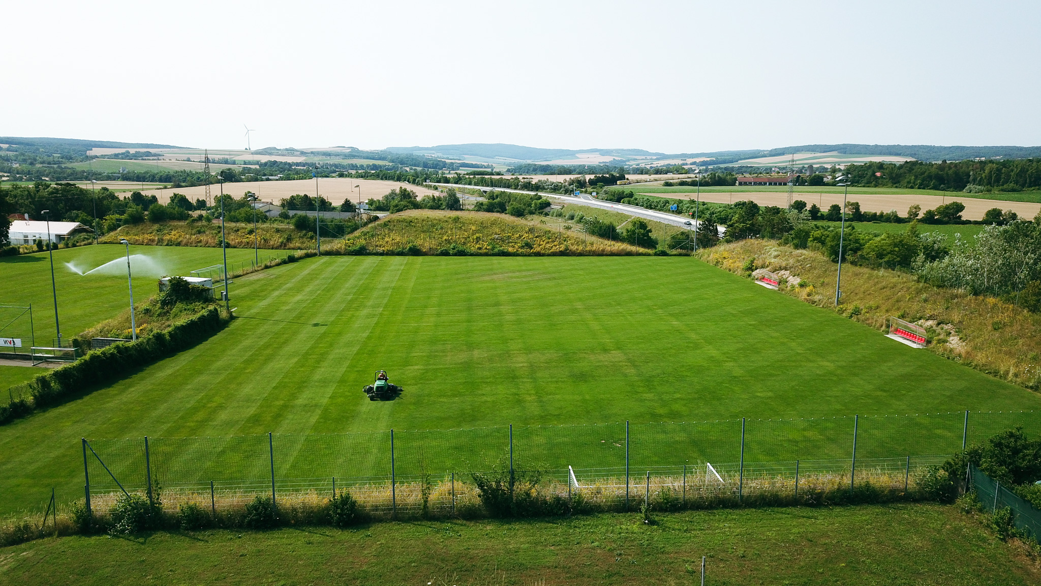 Fu&szlig;balltrainingsplatz in Nieder&ouml;sterreich, eingebettet in eine l&auml;ndliche Landschaft mit Blick auf Felder, Windr&auml;der und eine Landstra&szlig;e.