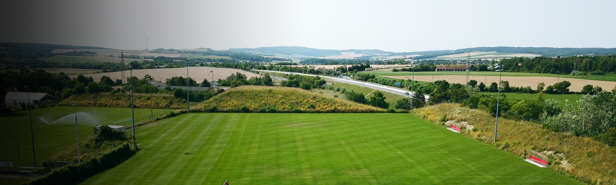 Fu&szlig;balltrainingsplatz in Nieder&ouml;sterreich, eingebettet in eine l&auml;ndliche Landschaft mit Blick auf Felder, Windr&auml;der und eine Landstra&szlig;e.