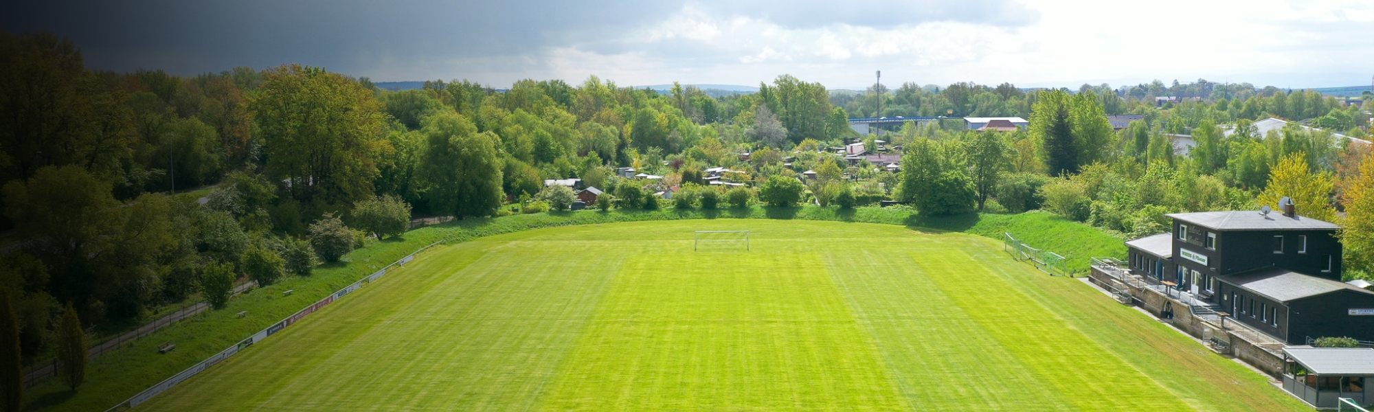 Luftaufnahme eines Fußballplatzes mit gepflegtem Rasen in Niedersachsen, umgeben von viel Grün, mit einem Vereinsheim auf der rechten Seite.
