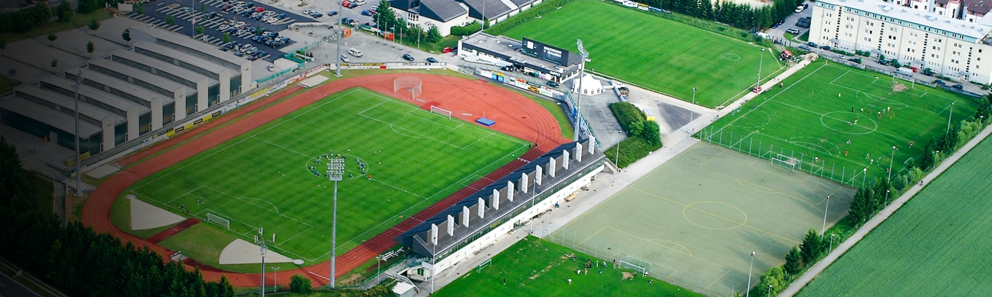 Sportzentrum in Ober&ouml;sterreich aus der Vogelperspektive mit Stadion, Trainingspl&auml;tzen und einer Laufbahn, eingebettet in eine st&auml;dtische Umgebung mit angrenzenden Feldern und Verkehrsstra&szlig;en.