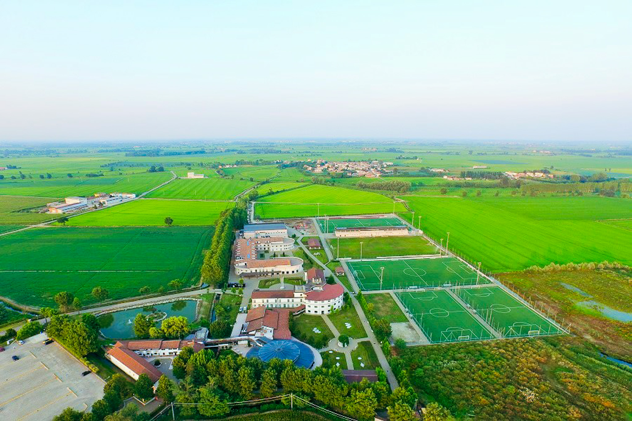 Luftaufnahme der Trainingsanlage im Piemont mit mehreren Fu&szlig;ballpl&auml;tzen, Sporthallen und Hotelgeb&auml;uden inmitten einer l&auml;ndlichen, gr&uuml;nen Landschaft.