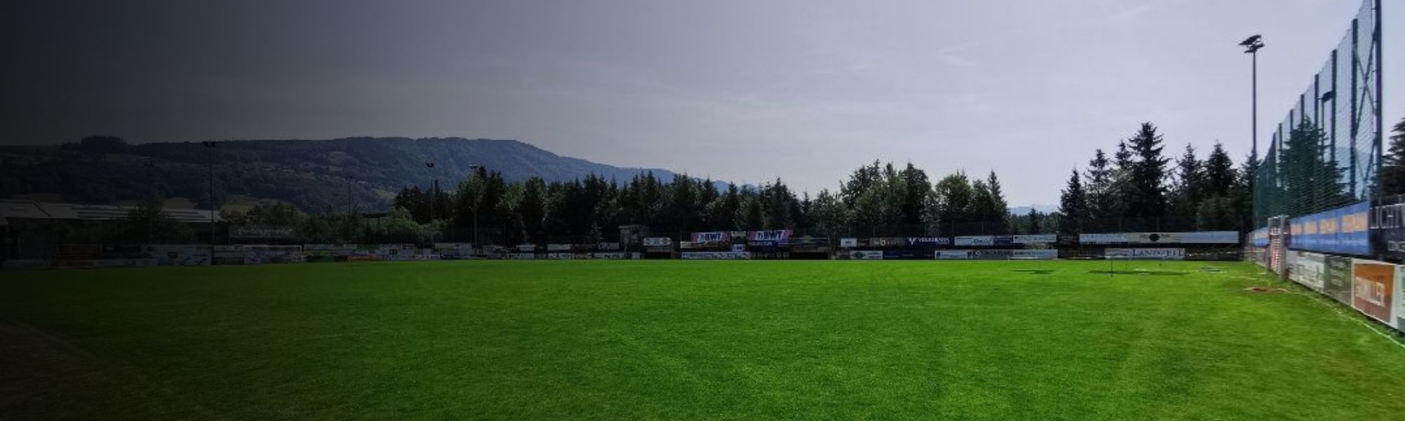 Kunstrasen-Fu&szlig;ballplatz auf Sardinien mit markierten Spielfeldlinien und Umz&auml;unung, im Hintergrund Berge und Geb&auml;ude.