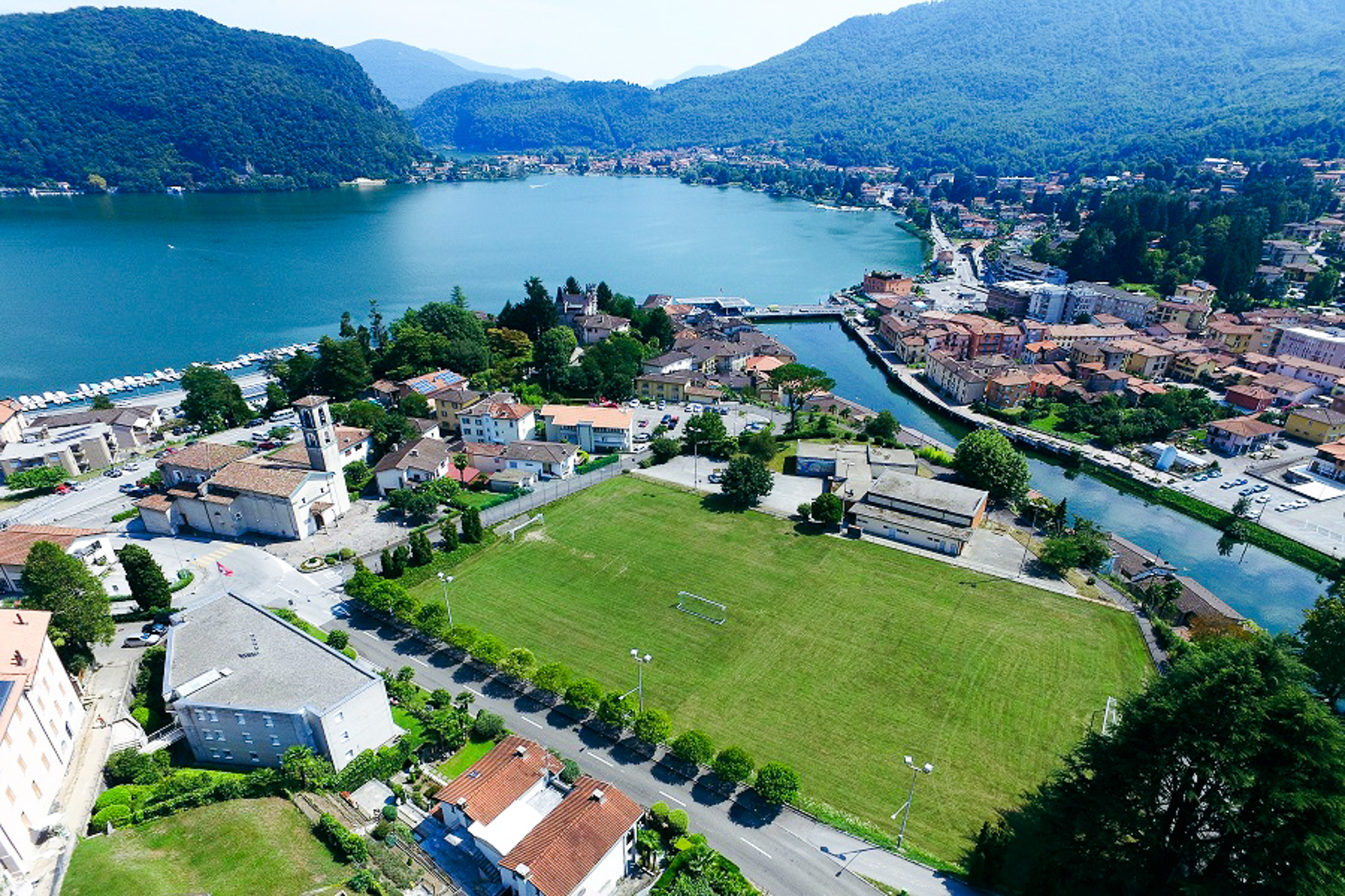 Fu&szlig;ballplatz in der Schweiz, umgeben von H&auml;usern und einem Fluss, mit Blick auf den See.